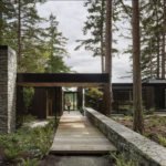 A modern Northwest-style home on Whidbey Island, featuring large glass windows, wood siding, and a minimalist design that integrates with the surrounding natural landscape. The home emphasizes sustainability and an indoor-outdoor connection.